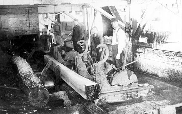 Photo of sawmill interior doggers and setters stand along a carriage that holds a cut log, ca. 1905.