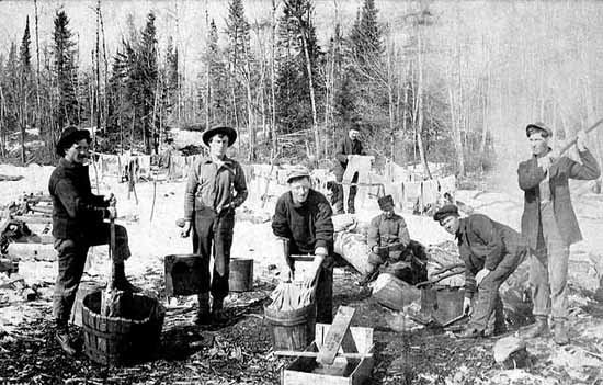 Photo of seven men doing their laundry outside in wooden buckets, in the background one man hangs his clean clothes on a clothes line, ca. 1910.